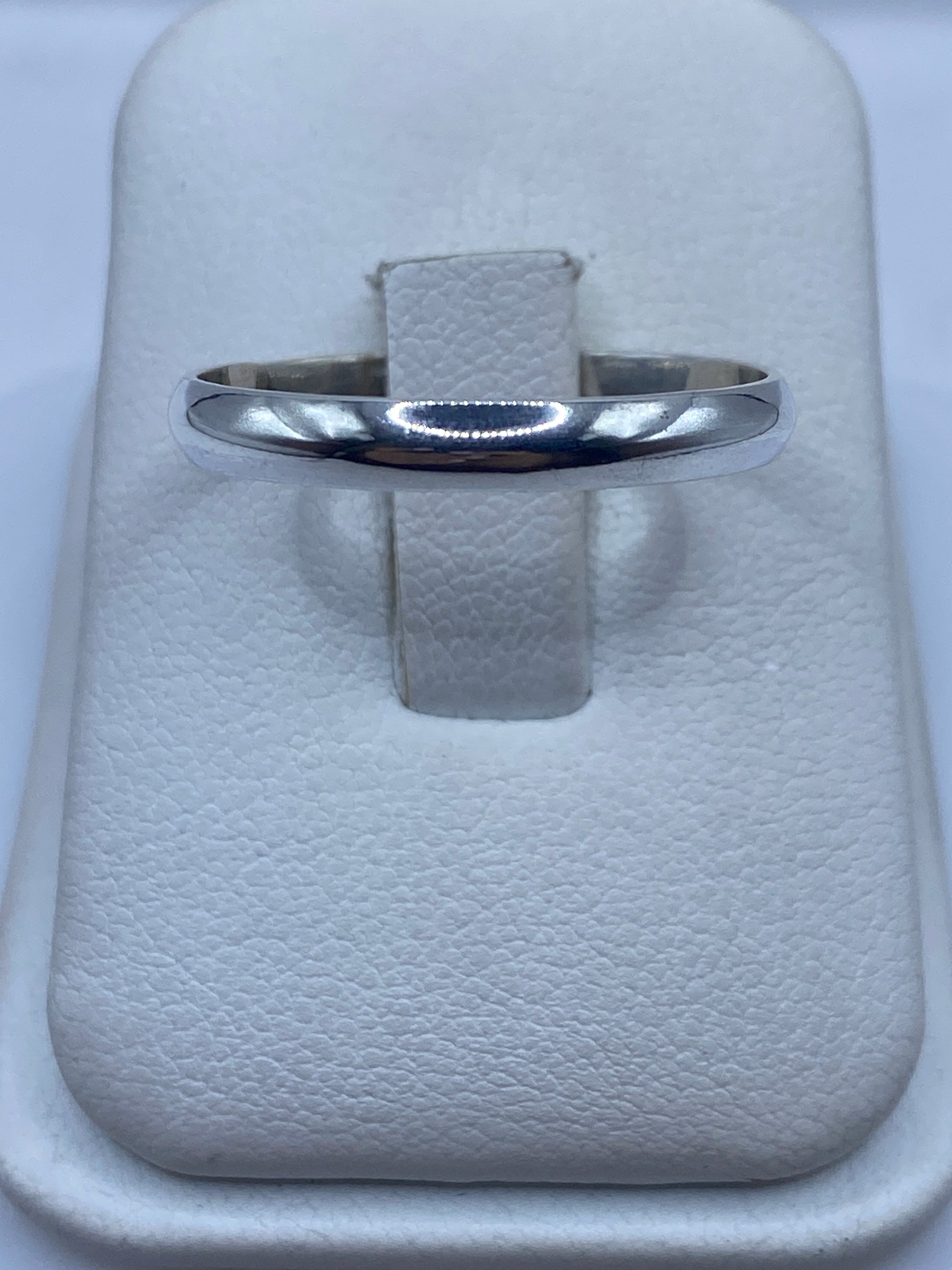 Anillo de plata banda pulida en estuche blanco, vista superior mostrando el brillo espejo