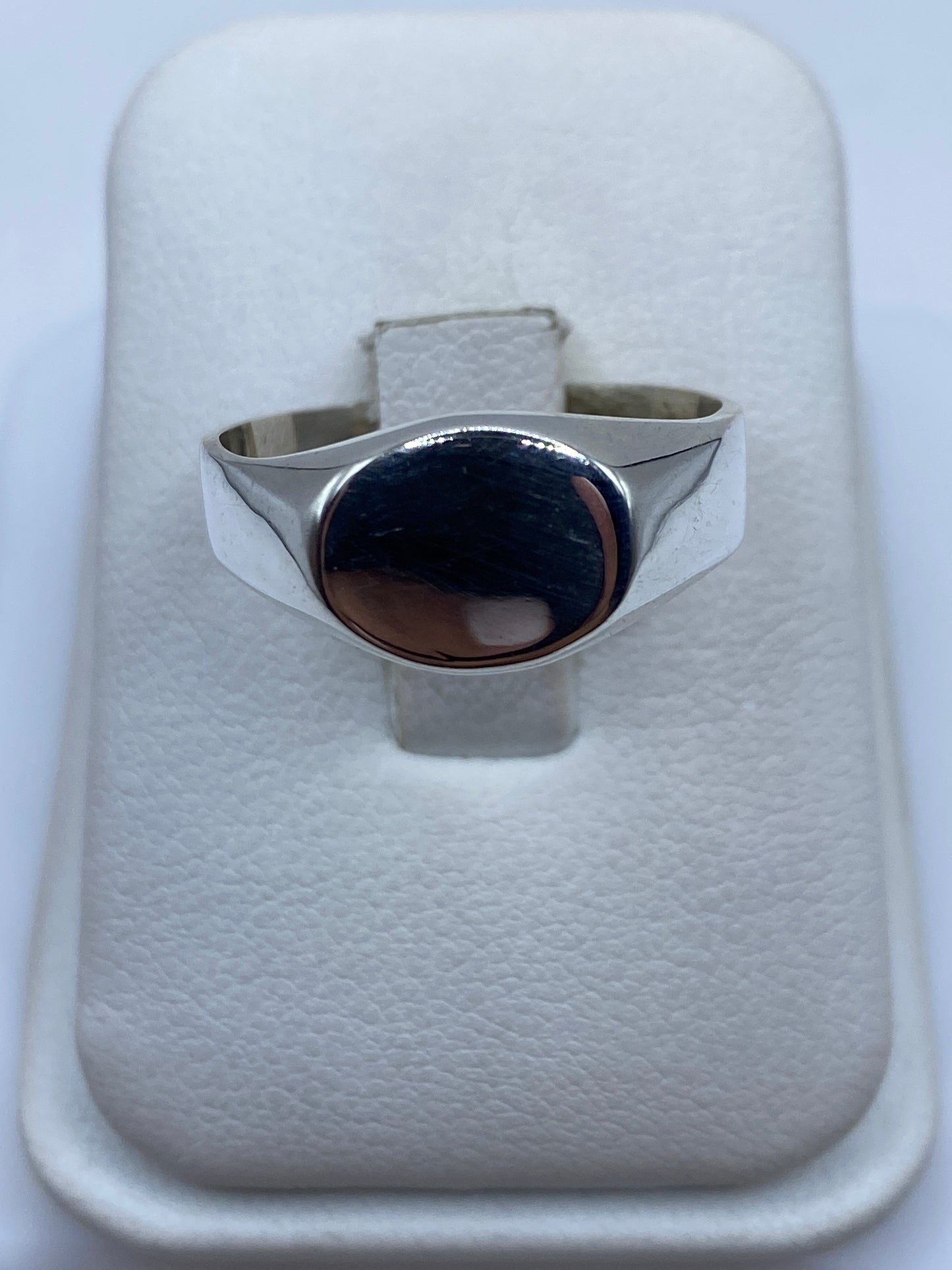 Anillo solitario de plata pulida sobre presentador blanco, vista frontal del engaste liso