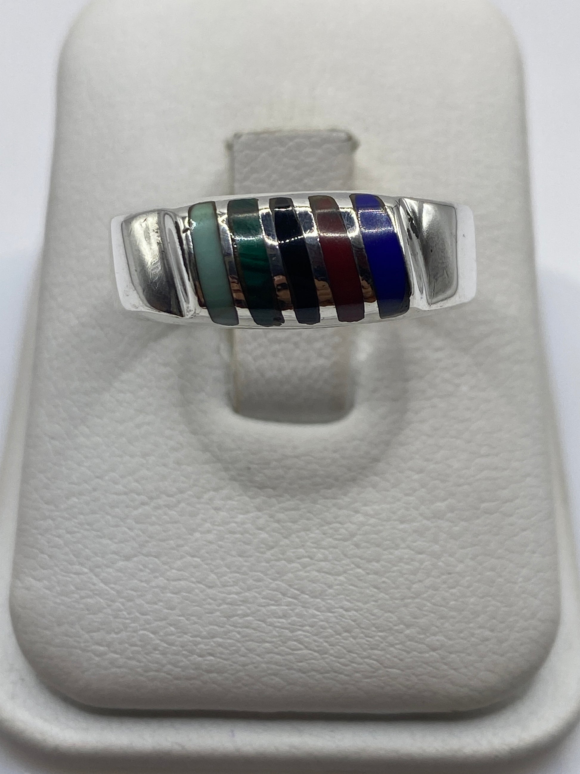 Anillo de plata con franjas de piedras multicolor (verde, negro, azul, bordo, blanco) en mano de persona