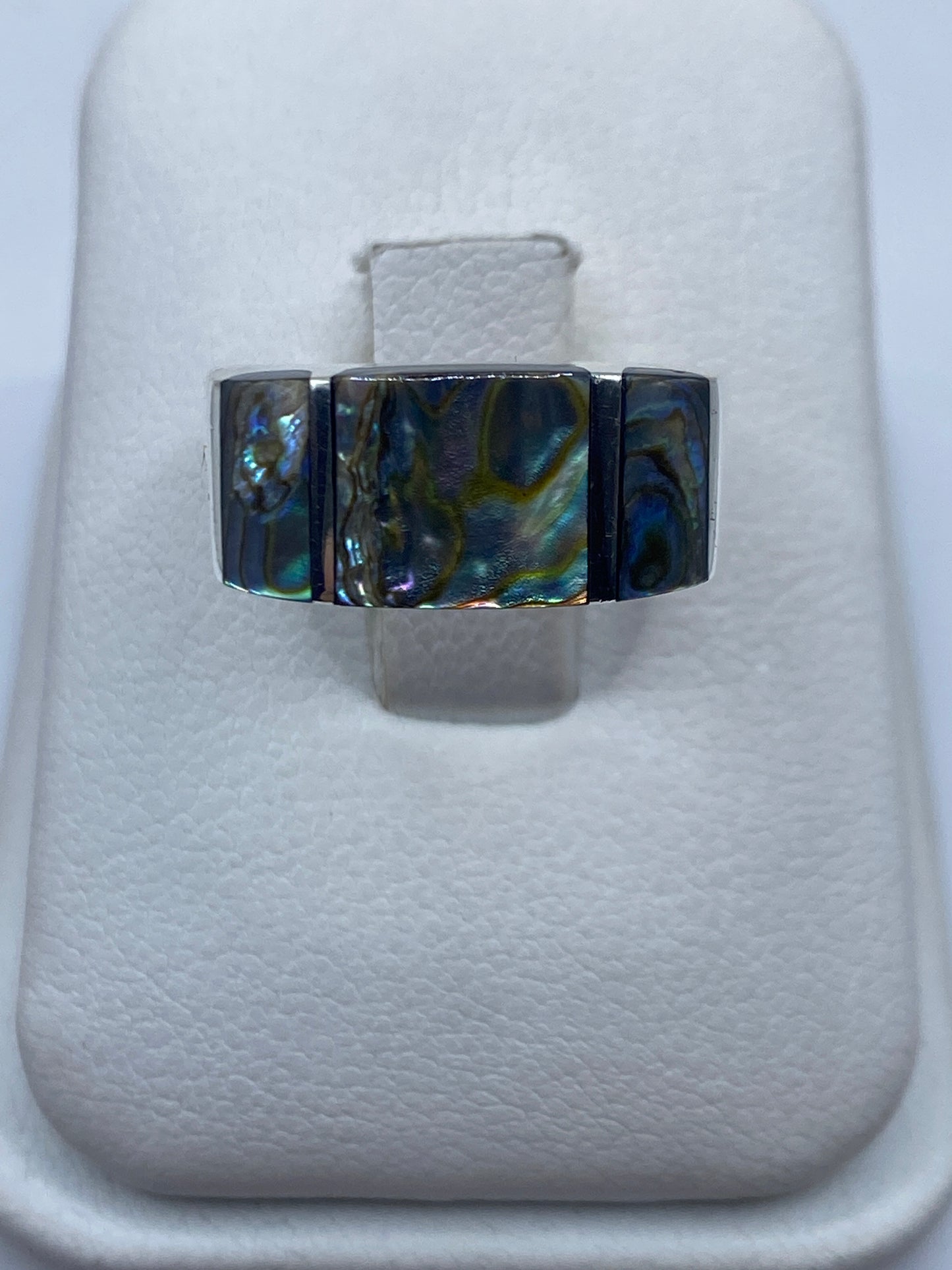 Anillo de plata geométrico con piedra iridiscente azul y verde sobre estuche blanco