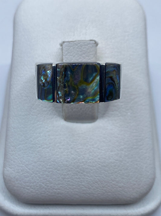 Anillo de plata geométrico con piedra iridiscente azul y verde sobre estuche blanco