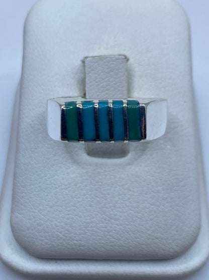 Anillo de plata con bandas escalonadas y piedras azul cielo, visto de frente sobre fondo blanco