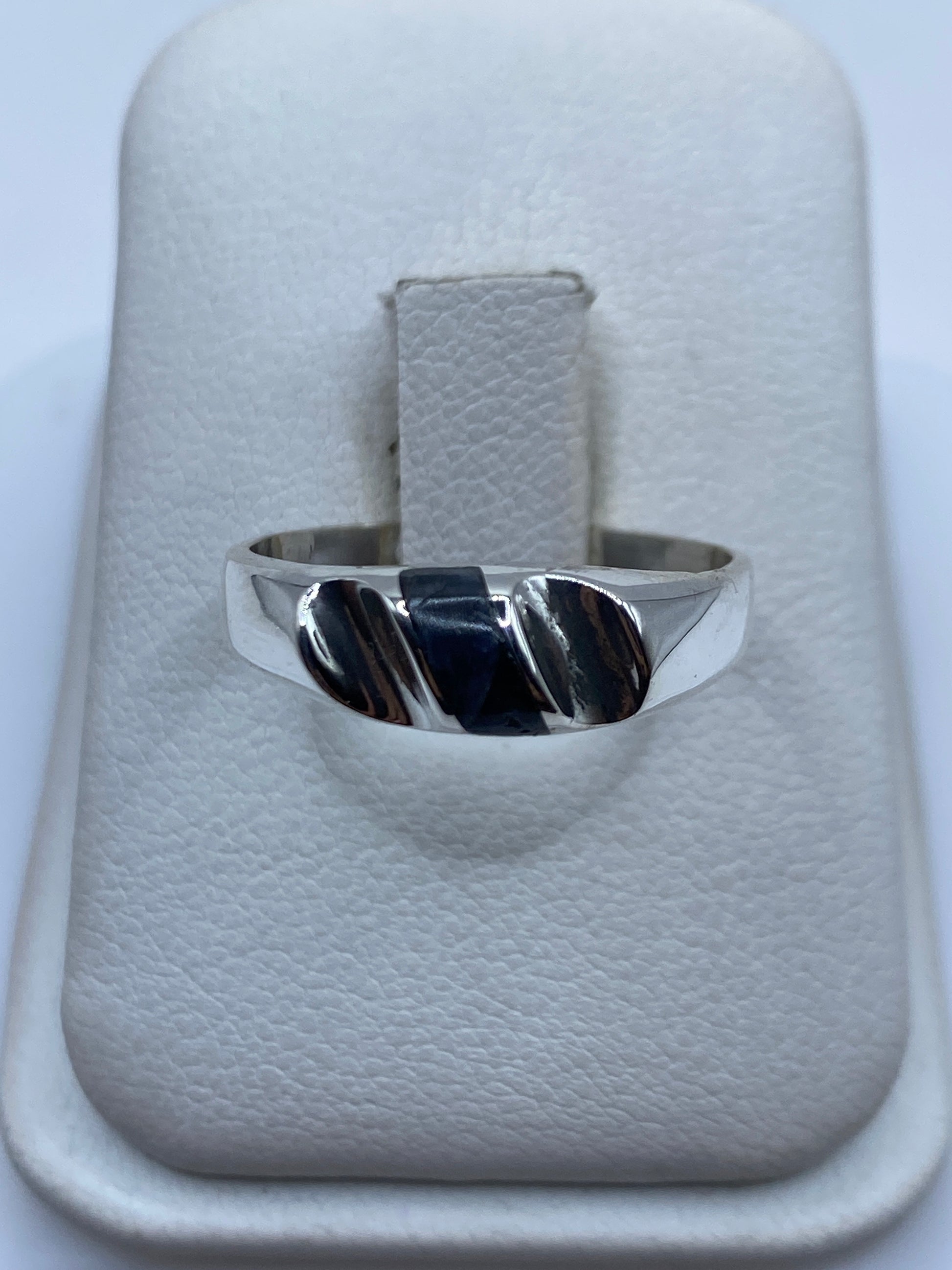 Anillo de plata con onix negro sobre almohada blanca, vista frontal del diseño minimalista