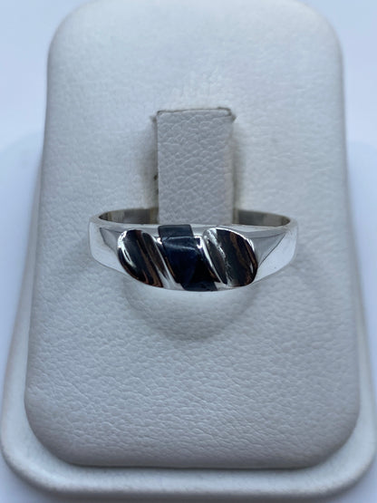 Anillo de plata con onix negro sobre almohada blanca, vista frontal del diseño minimalista