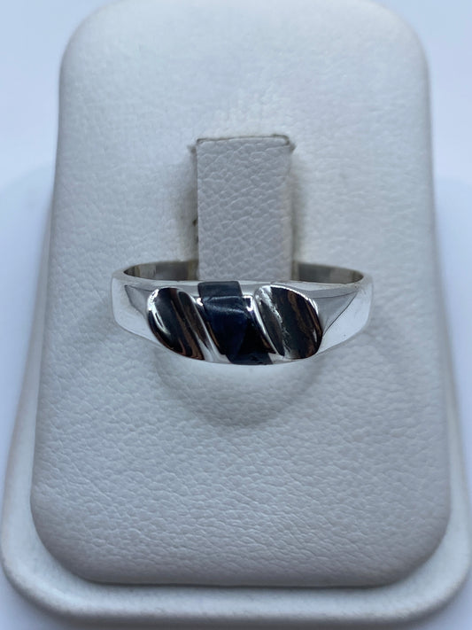 Anillo de plata con onix negro sobre almohada blanca, vista frontal del diseño minimalista