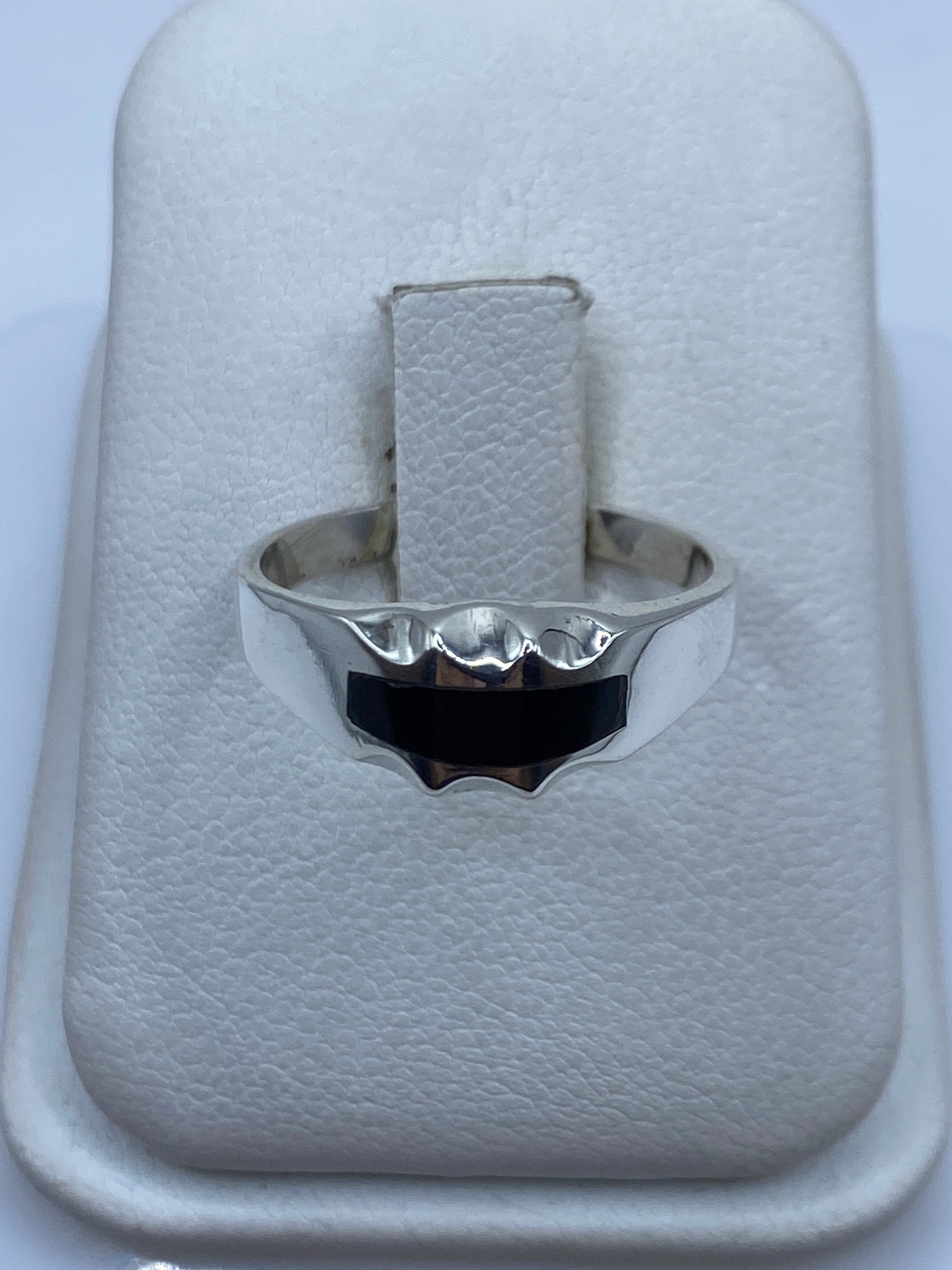 Anillo de plata con ónix negro pulido en estuche blanco, vista frontal mostrando la banda ondulante