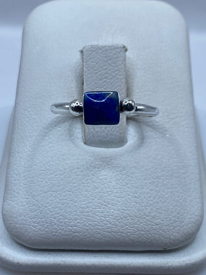 Anillo de plata .950 solitario con piedra azul cuadrada y esferas laterales, mostrado en estuche blanco