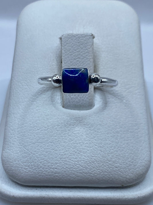 Anillo de plata .950 solitario con piedra azul cuadrada y esferas laterales, mostrado en estuche blanco