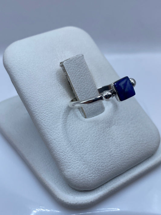 Vista frontal del anillo minimalista con piedra azul en mano de mujer