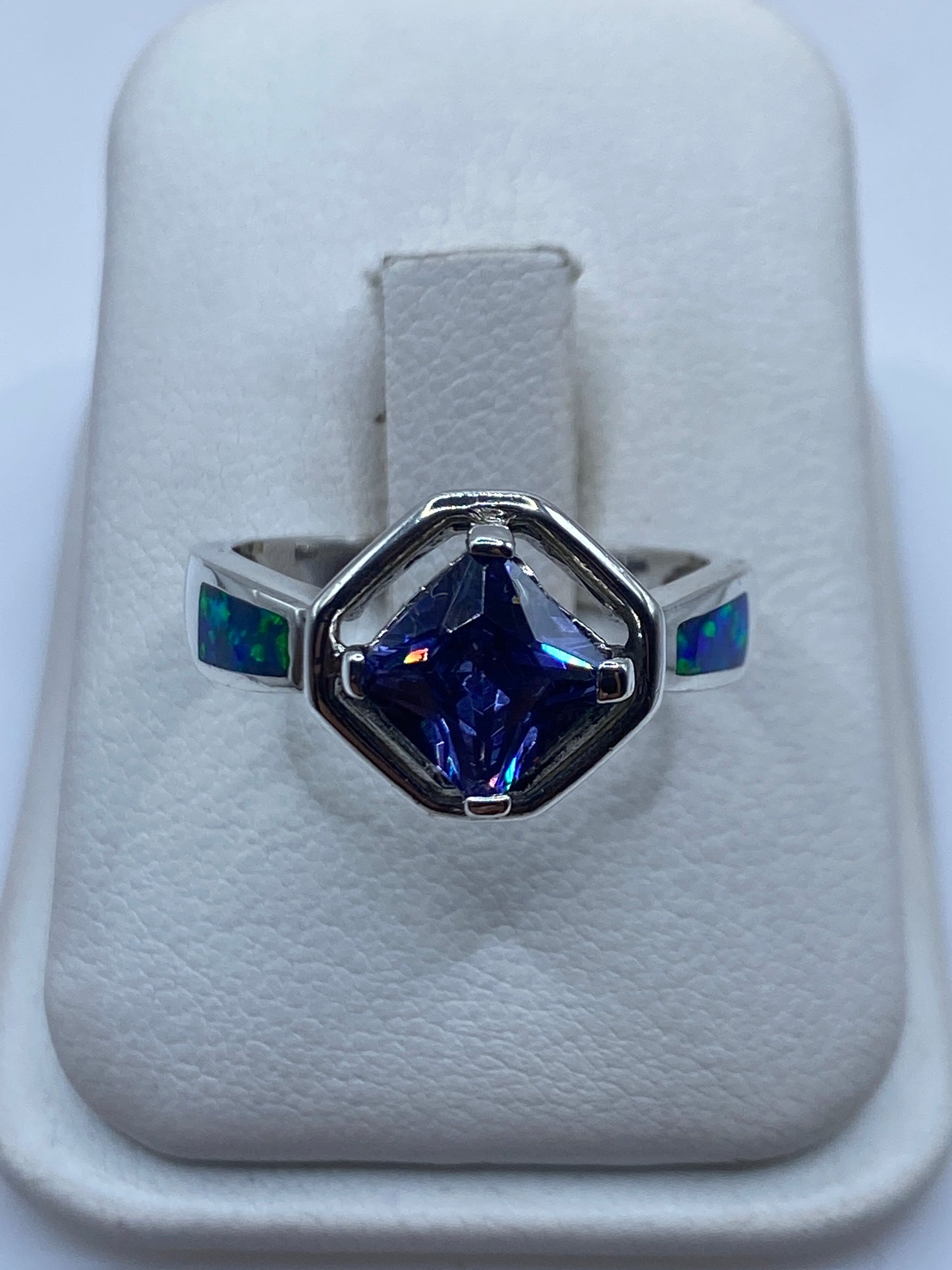 Anillo de plata con ópalo de fuego azul en caja blanca, vista frontal mostrando el brillo de la piedra