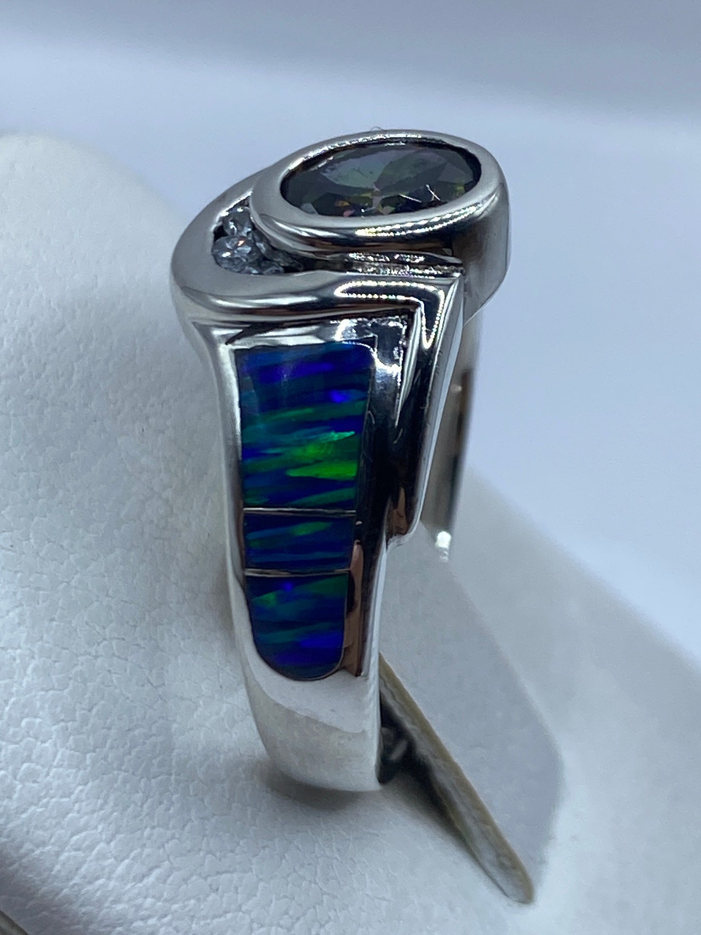 Anillo ópalo de fuego en la mano, con juego de colores azules y verdes bajo luz natural