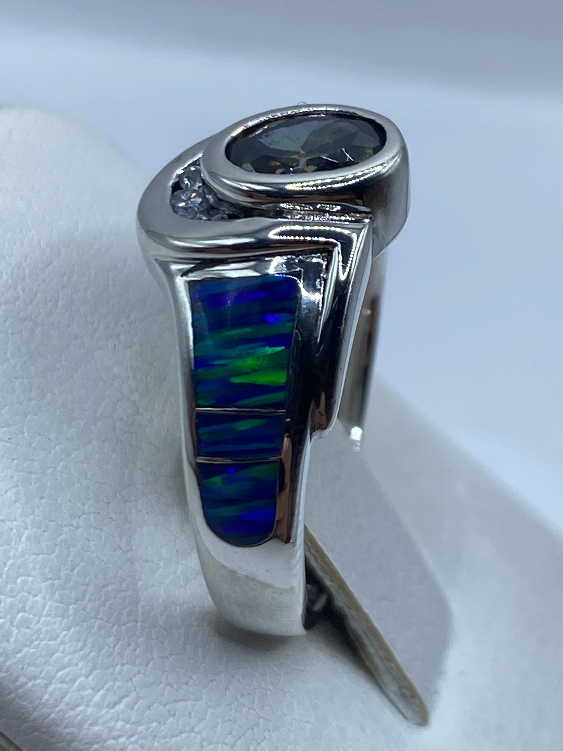 Anillo ópalo de fuego en la mano, con juego de colores azules y verdes bajo luz natural
