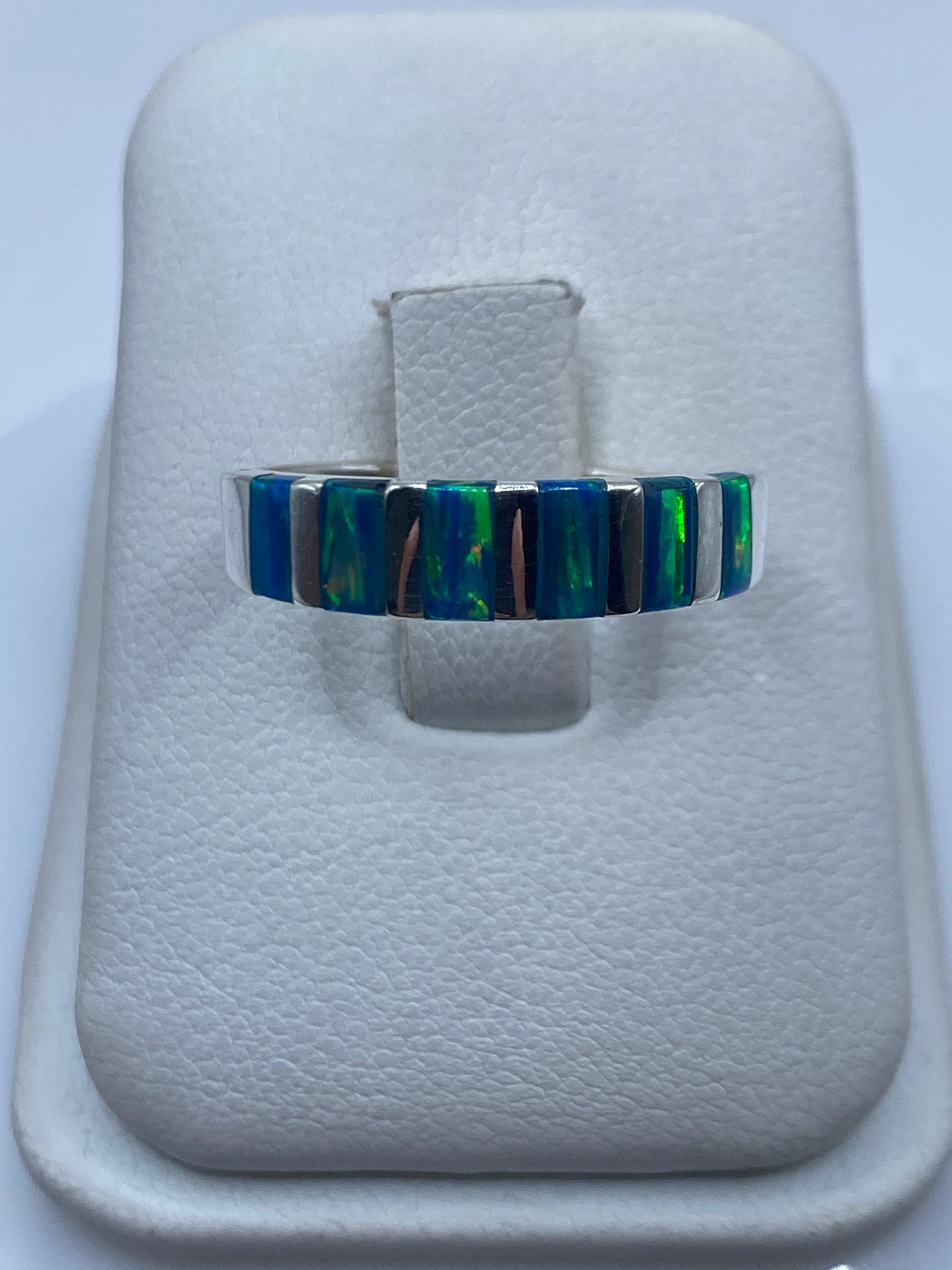 Anillo de plata con banda alternada de ópalo de fuego azul y verde en dedo de mujer