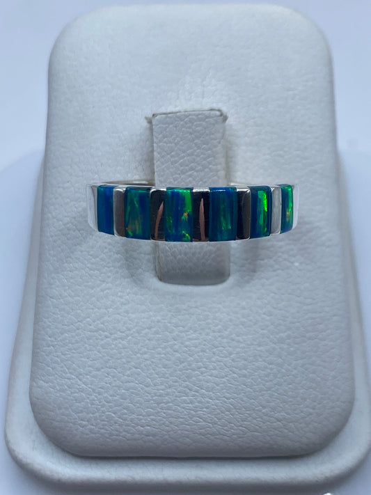 Anillo de plata con banda alternada de ópalo de fuego azul y verde en dedo de mujer