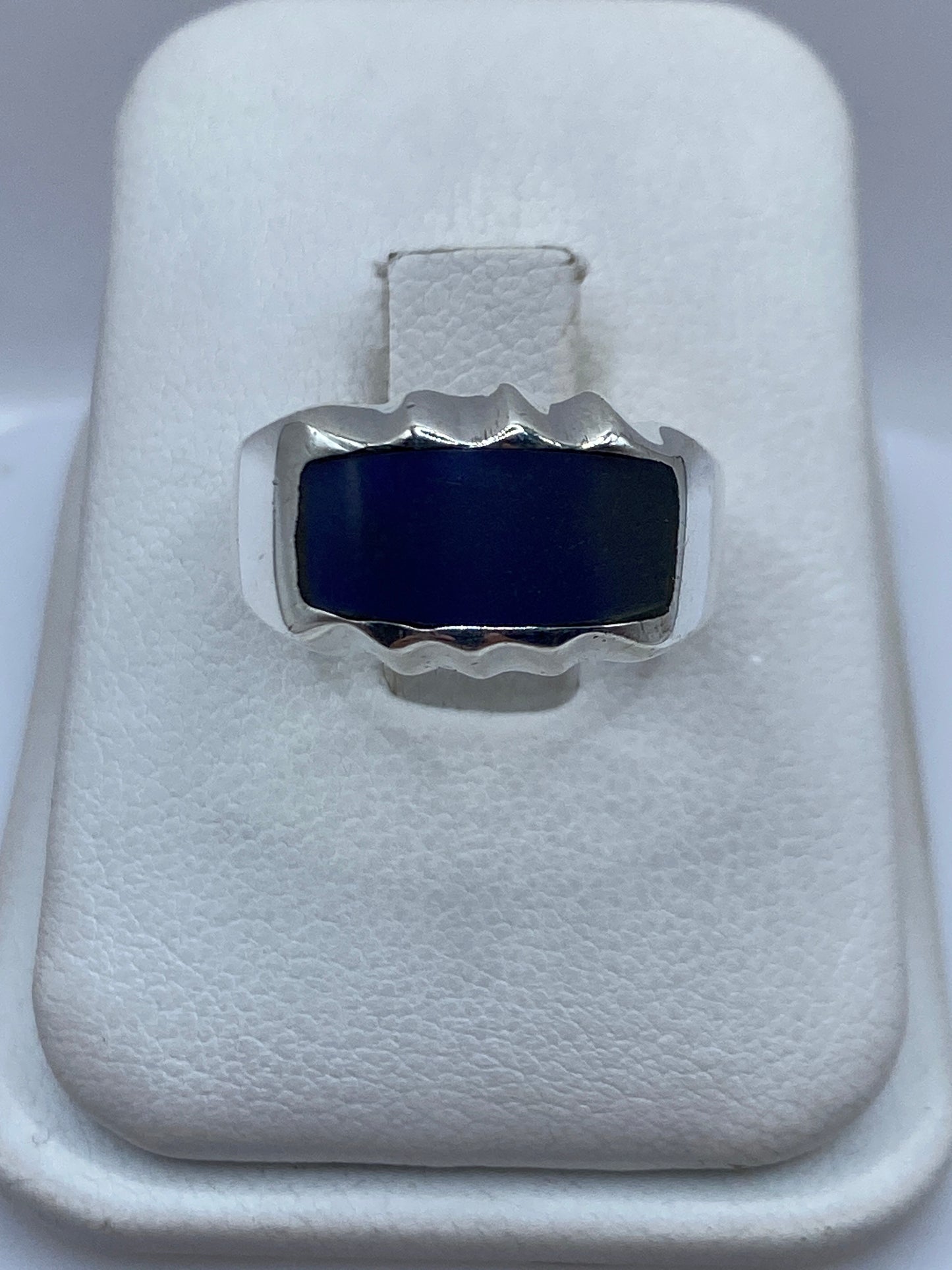 Anillo de plata con onix azul profundo y marco ondulante en la mano de una persona