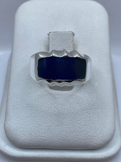 Anillo de plata con onix azul profundo y marco ondulante en la mano de una persona