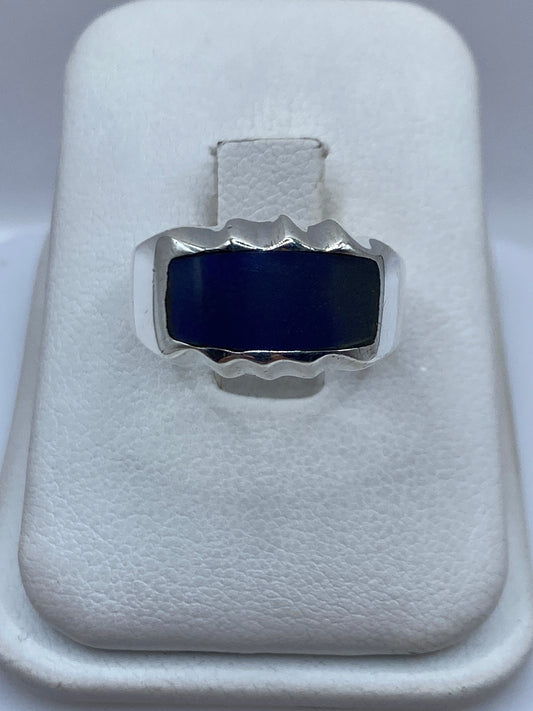 Anillo de plata con onix azul profundo y marco ondulante en la mano de una persona