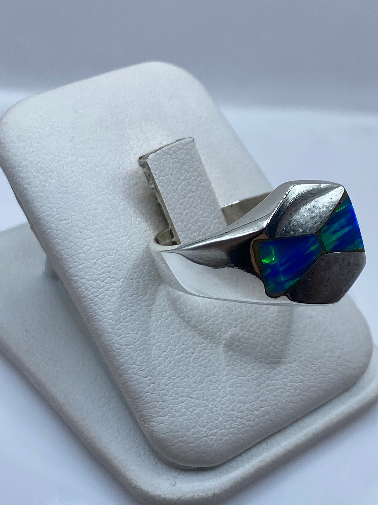 Vista frontal del anillo mostrando el juego de colores azul y verde del ópalo en la mano