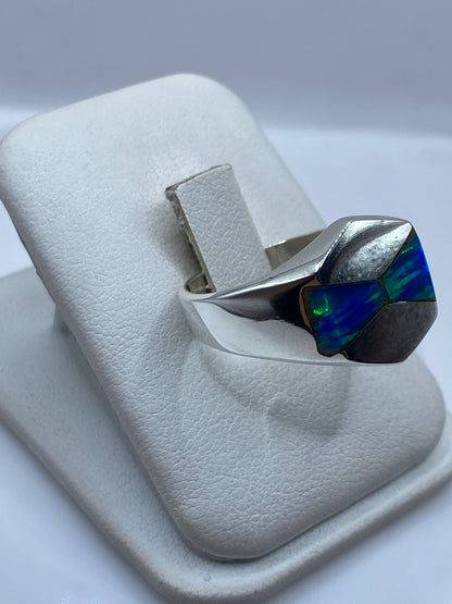 Vista frontal del anillo mostrando el juego de colores azul y verde del ópalo en la mano
