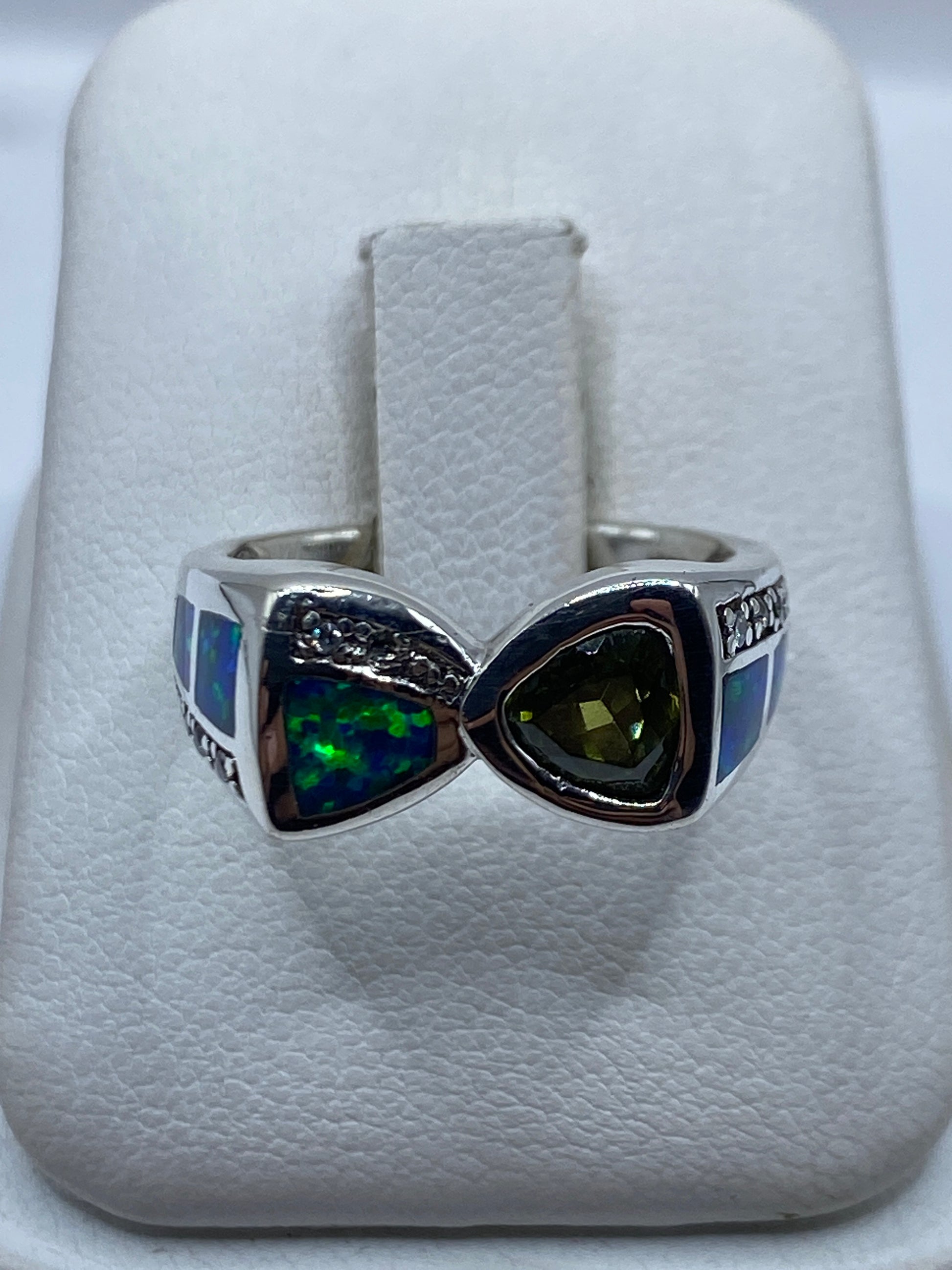 Anillo de plata con ópalo de fuego azul en forma de nudo geométrico, sobre almohada blanca