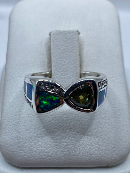 Anillo de plata con ópalo de fuego azul en forma de nudo geométrico, sobre almohada blanca