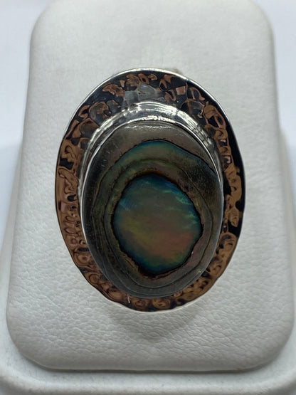 Anillo ajustable de plata con piedra iridiscente que cambia de color, visto desde arriba con reflejos azules y verdes