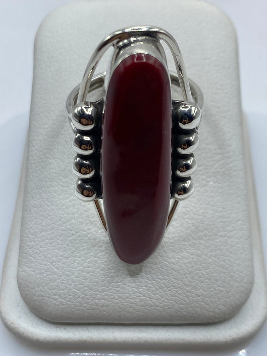 Anillo de plata con coral rojo ovalado y esferas decorativas en mano de mujer