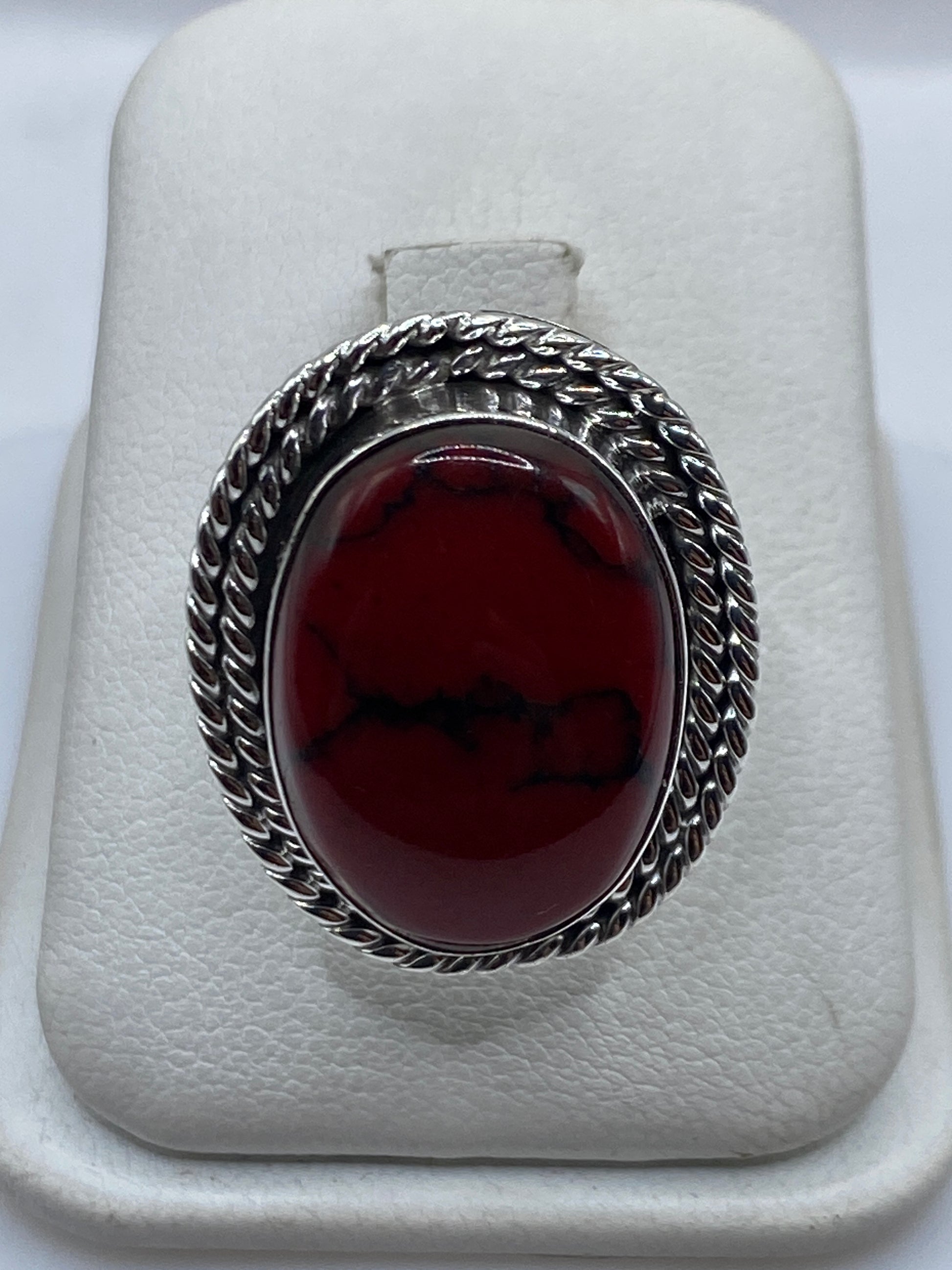 Anillo de plata con coral rojo natural en la mano de una mujer, mostrando la banda retorcida
