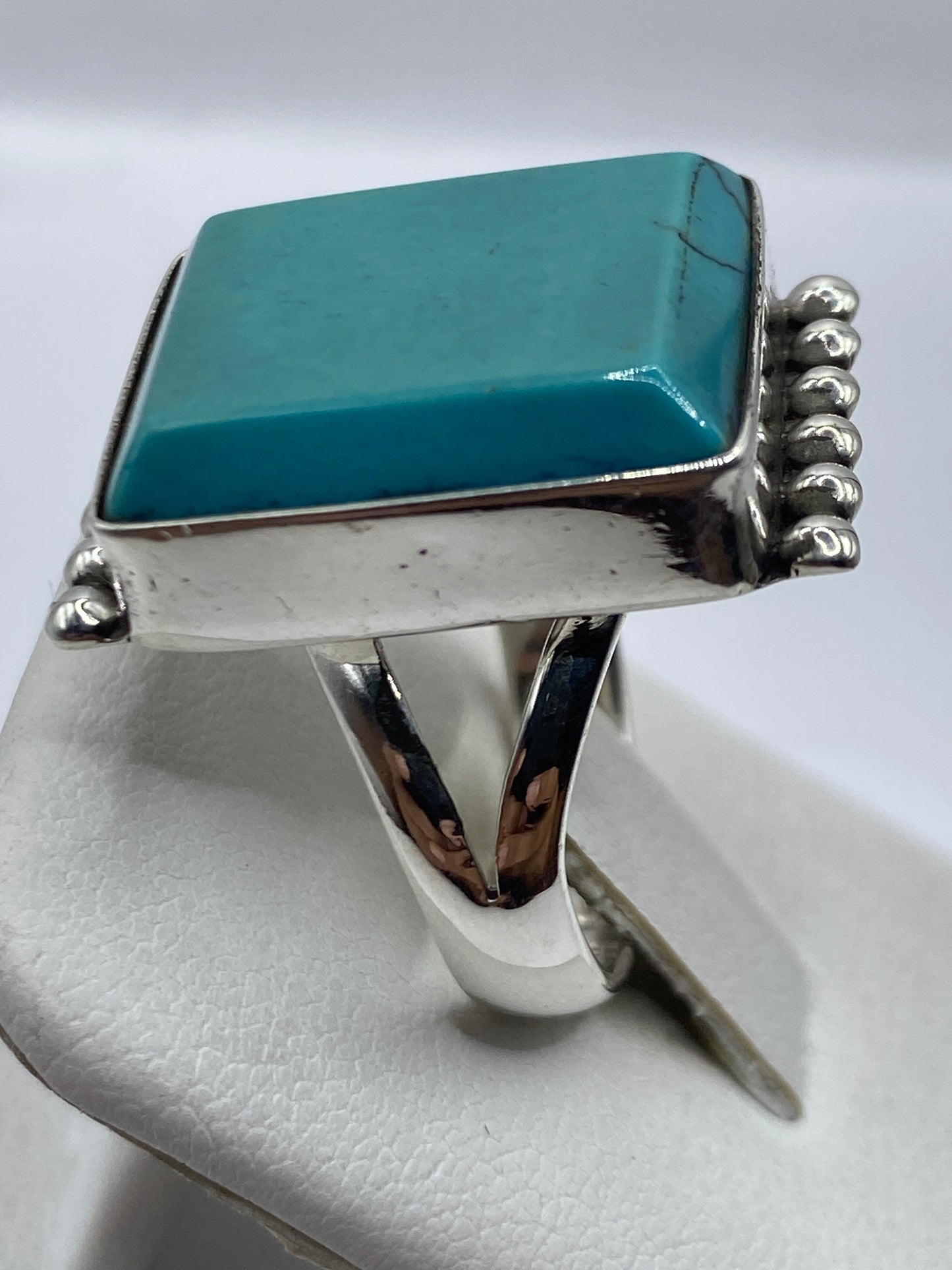 Detalle lateral del anillo de turquesa en mano, destacando las esferas de plata