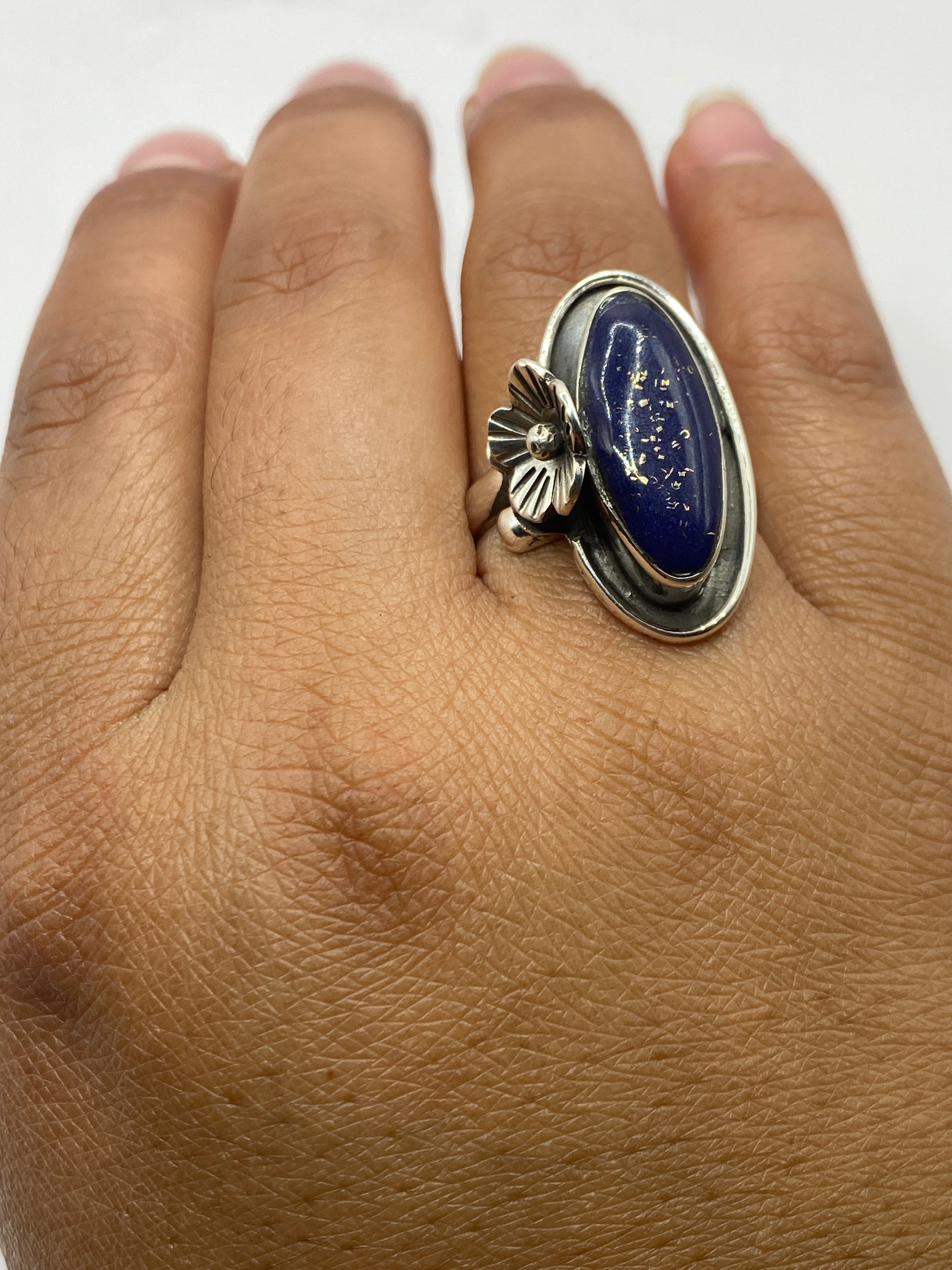Anillo con flor de plata en mano de mujer, lapislázuli brillante bajo luz natural