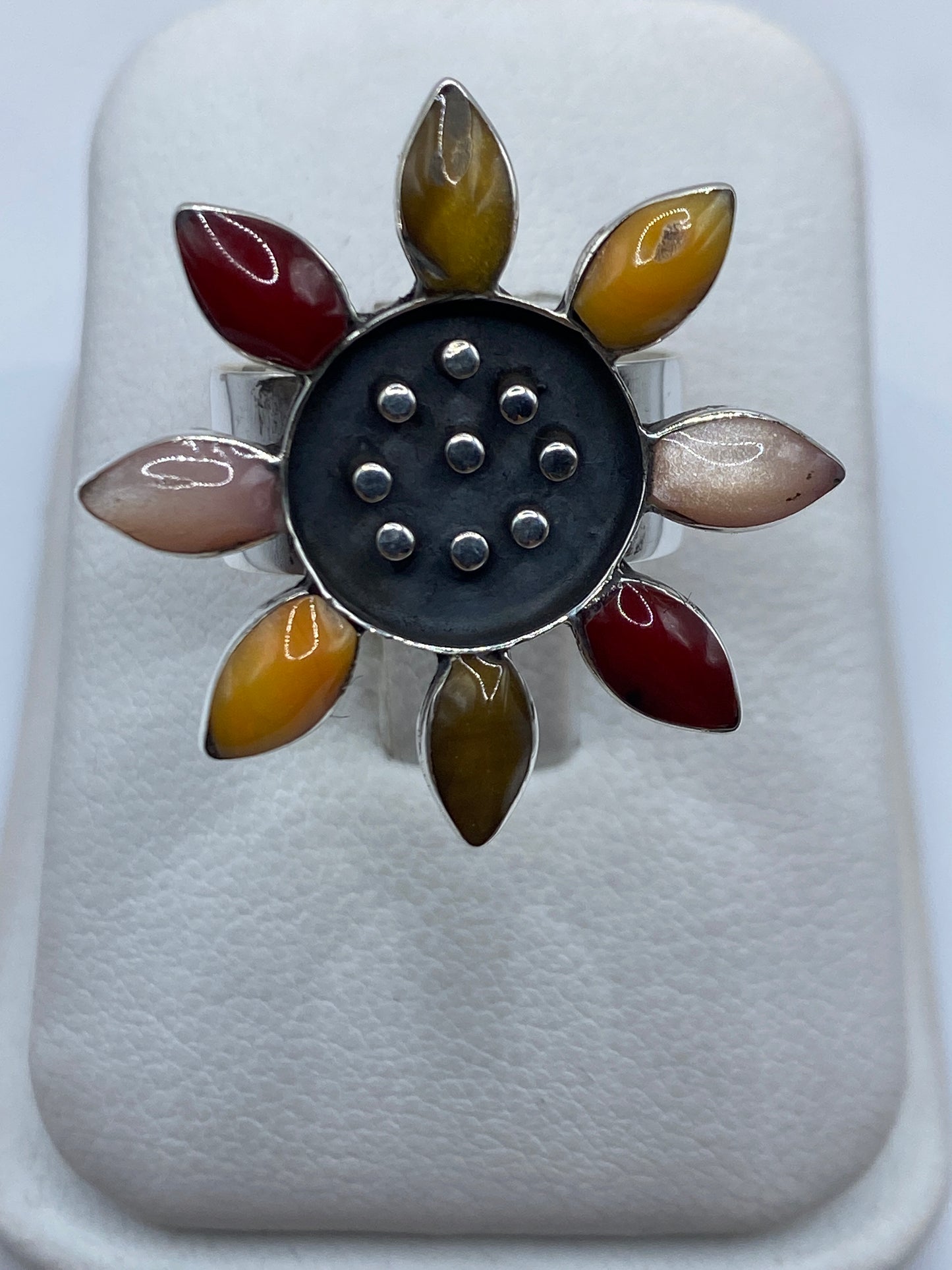 Anillo floral de plata con ocho pétalos de piedras naturales multicolor en la mano de una mujer