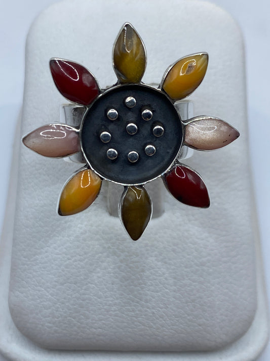 Anillo floral de plata con ocho pétalos de piedras naturales multicolor en la mano de una mujer