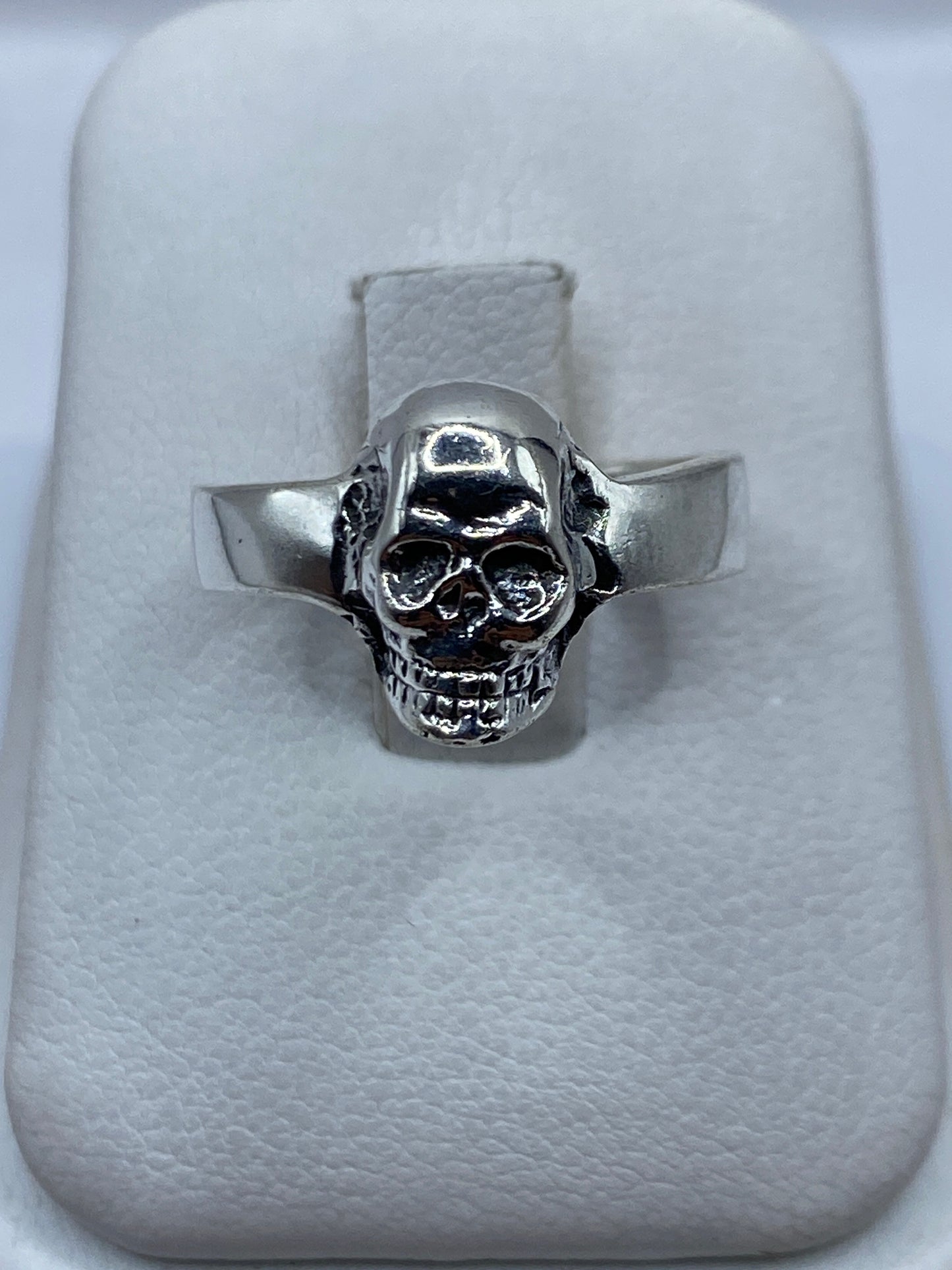 Anillo de plata calavera clásica, banda ancha pulida, vista frontal sobre cojín blanco