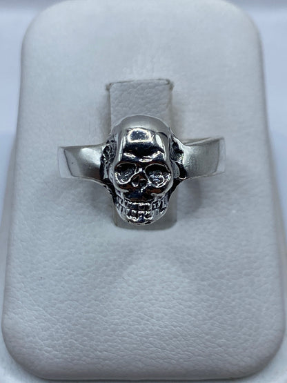 Anillo de plata calavera clásica, banda ancha pulida, vista frontal sobre cojín blanco