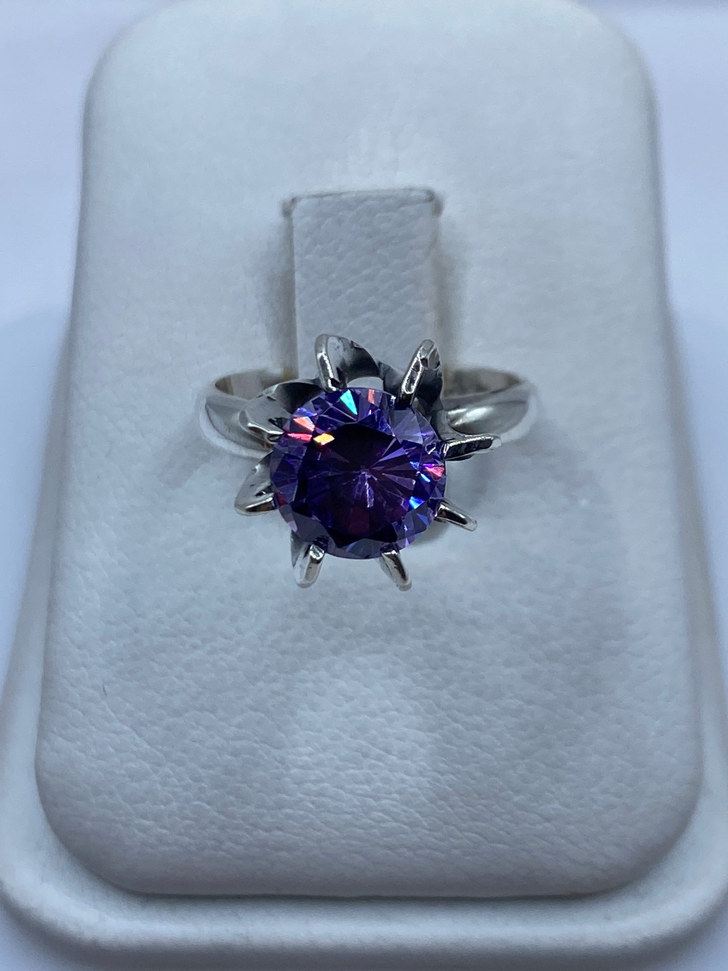Anillo solitario de plata .925 con circonia morada facetada, visto desde arriba sobre cojín blanco