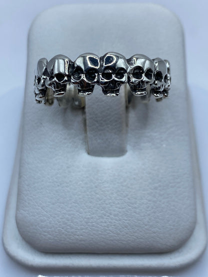 Anillo de plata con calaveras encadenadas visto desde arriba sobre fondo blanco