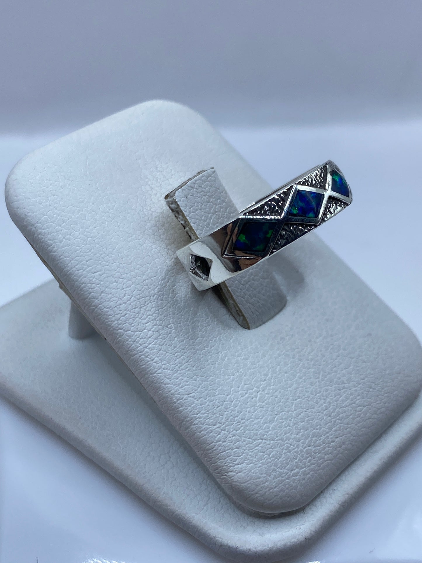 Anillo ópalo de fuego en plata sobre dedo mostrando el juego de colores azules y verdes