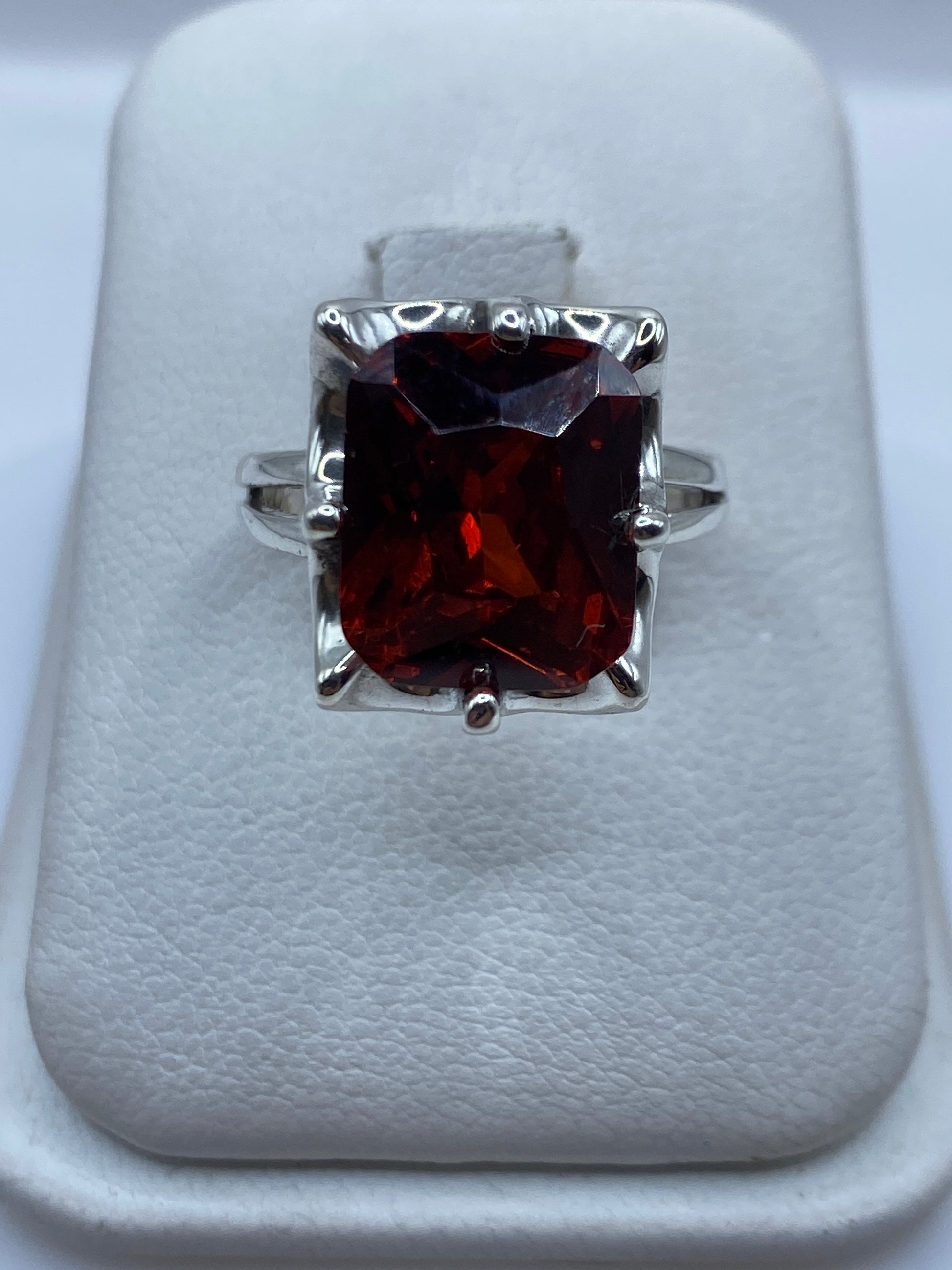 Anillo de plata solitario con circonia naranja en estuche blanco mostrando el brillo de la piedra