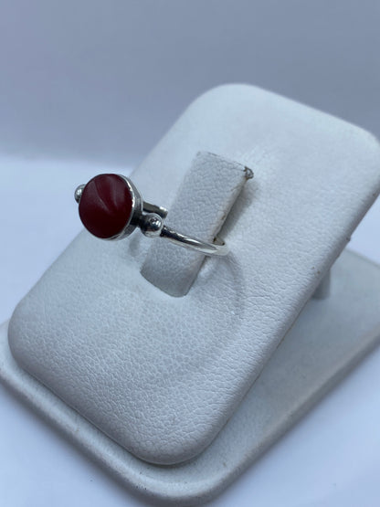 Anillo solitario de plata con piedra roja visto de lado mostrando bolitas laterales