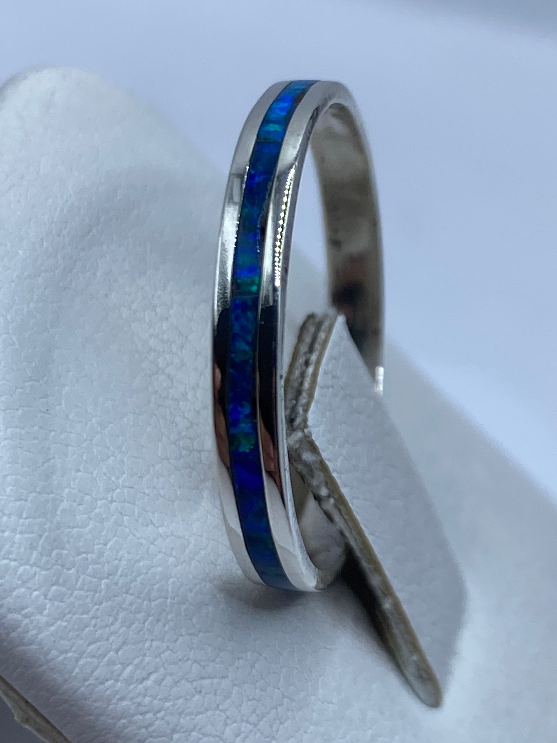 Anillo ópalo azul en dedo de mujer, luz natural resaltando el brillo de la piedra