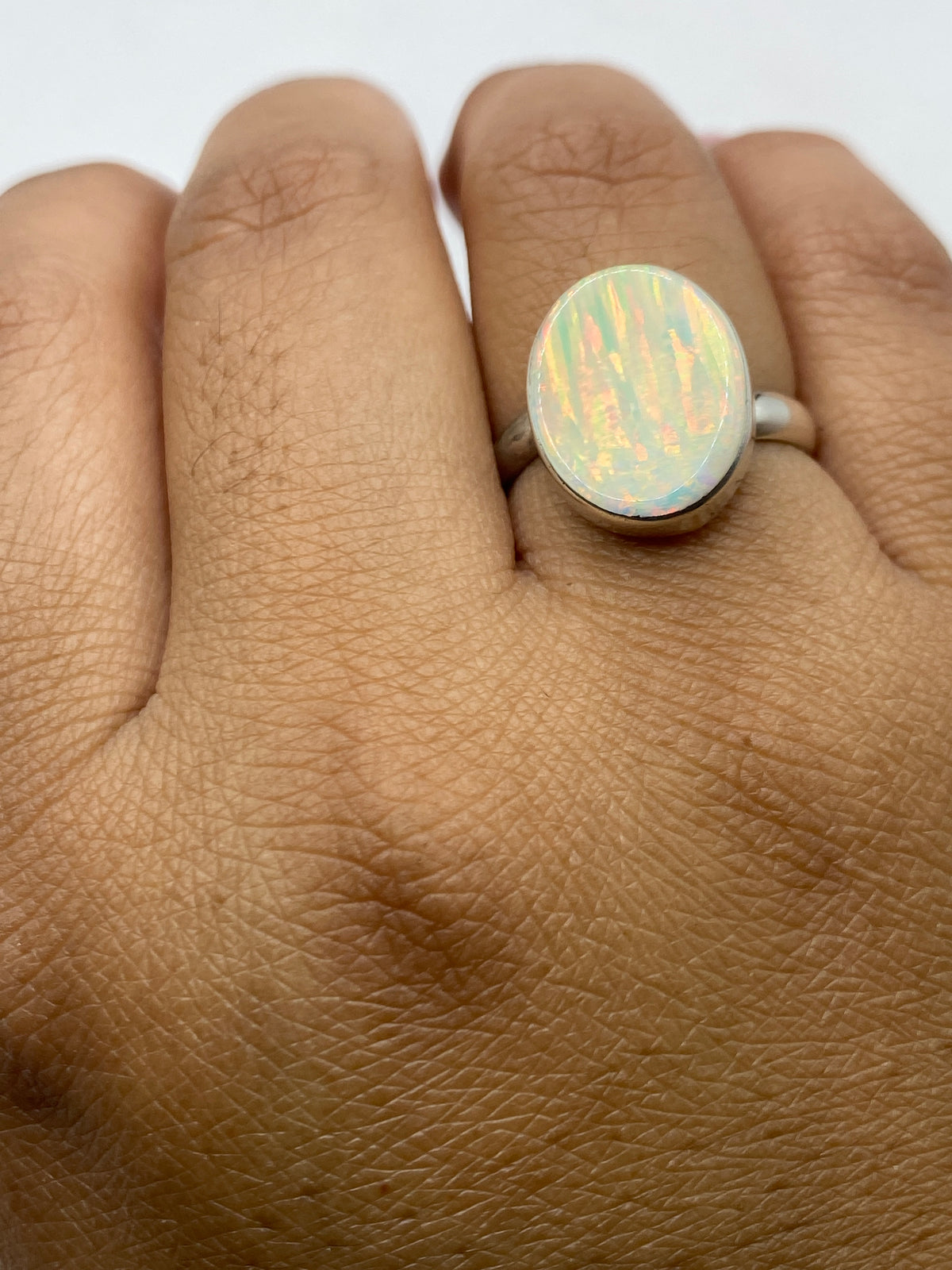 Anillo ajustable de ópalo de fuego en mano de mujer mostrando el juego de colores único