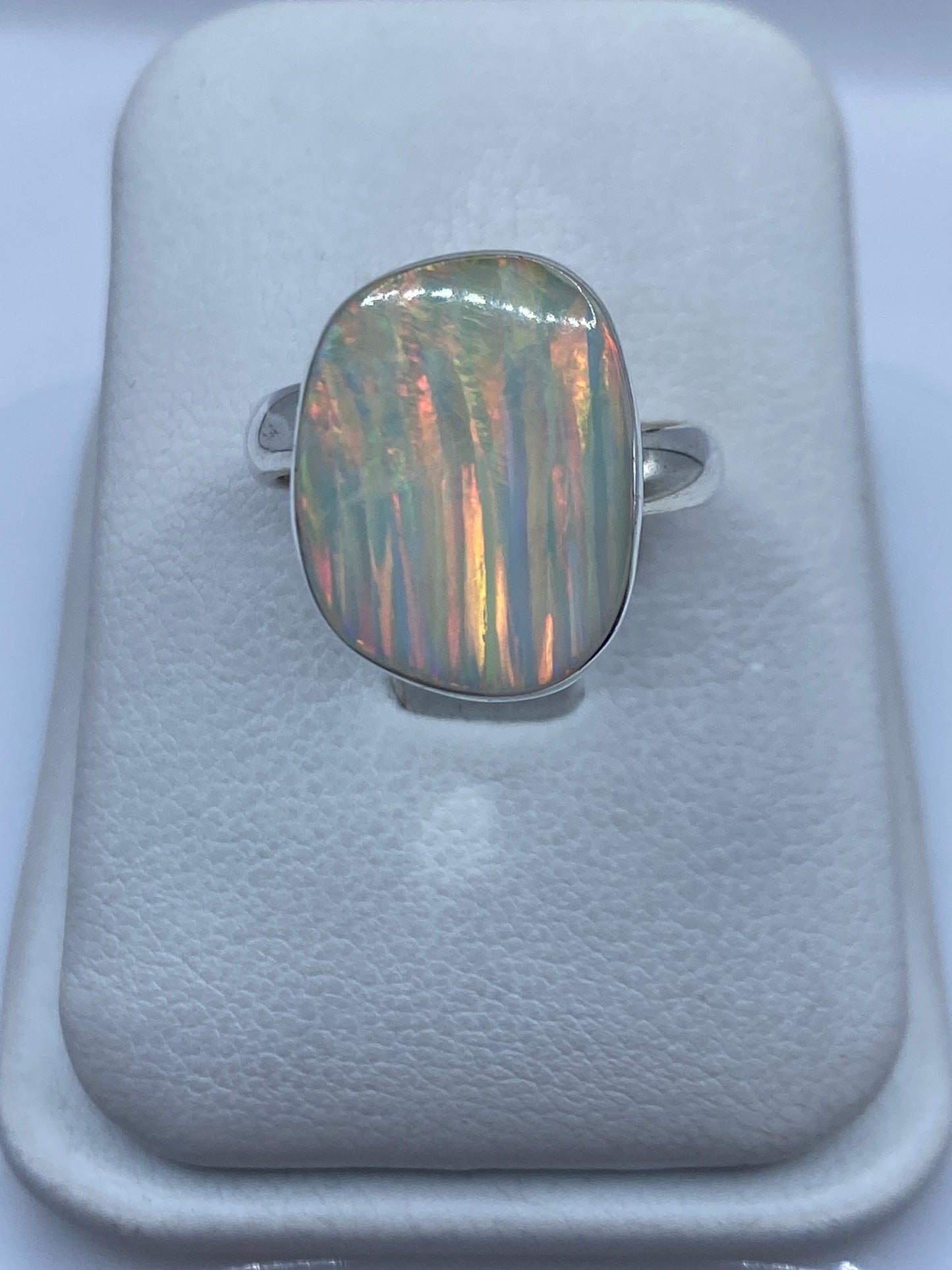 Anillo de plata con ópalo de fuego multicolor en mano de mujer, mostrando reflejos rojo-naranja