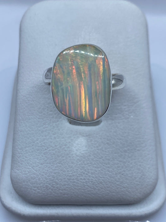 Anillo de plata con ópalo de fuego multicolor en mano de mujer, mostrando reflejos rojo-naranja
