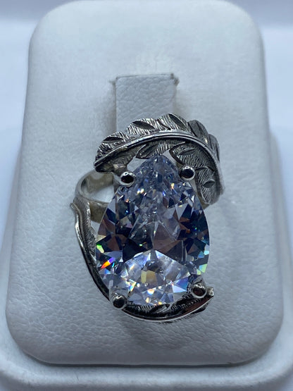Anillo de plata solitario con circonia blanca sobre almohada blanca, vista frontal mostrando el fuego de la piedra