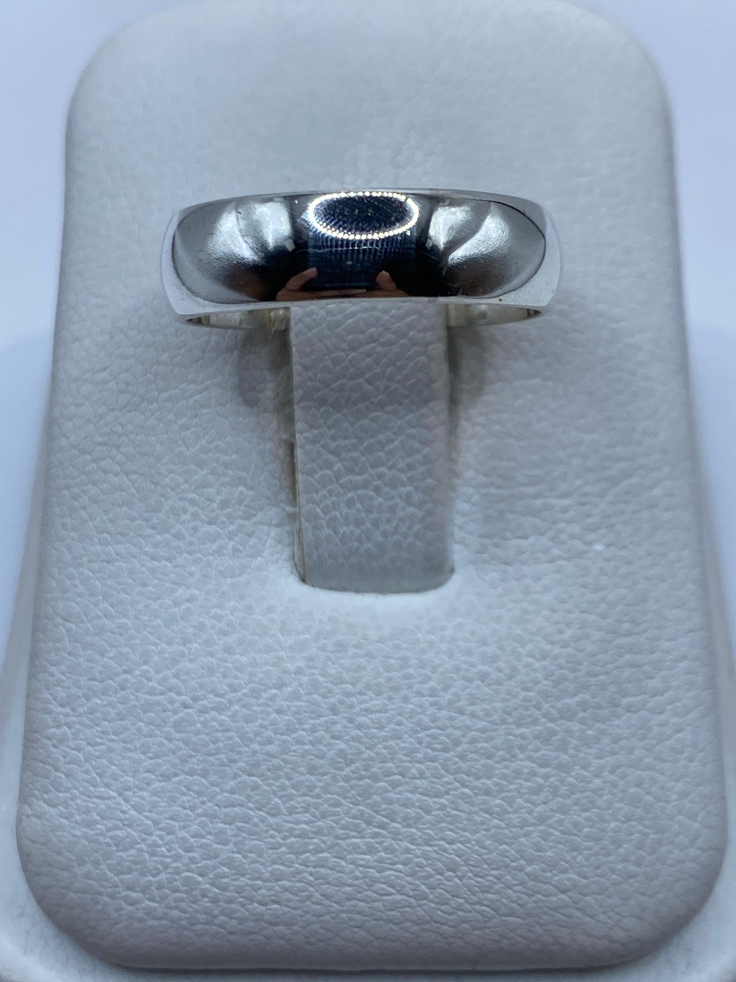 Anillo de plata lisa pulida en una mano, vista frontal de la banda minimalista