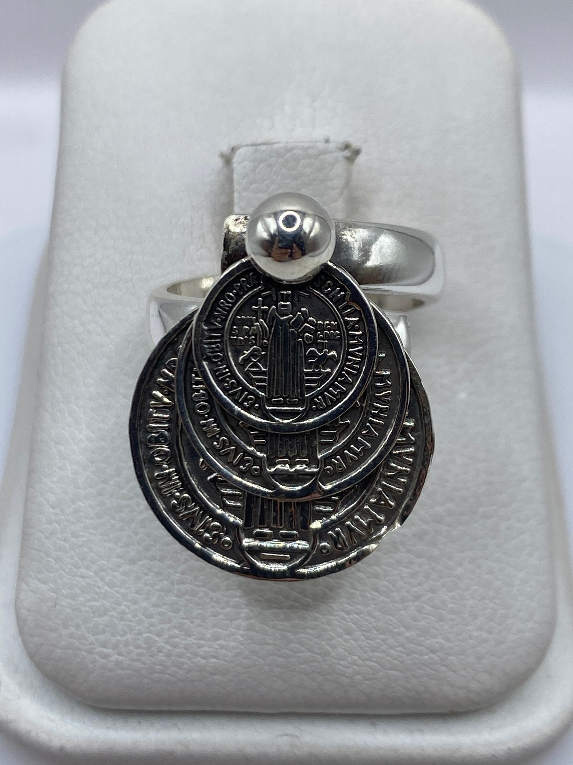 Anillo religioso de plata .925 ajustable sobre estuche blanco, visto de frente con detalle de diseño sagrado