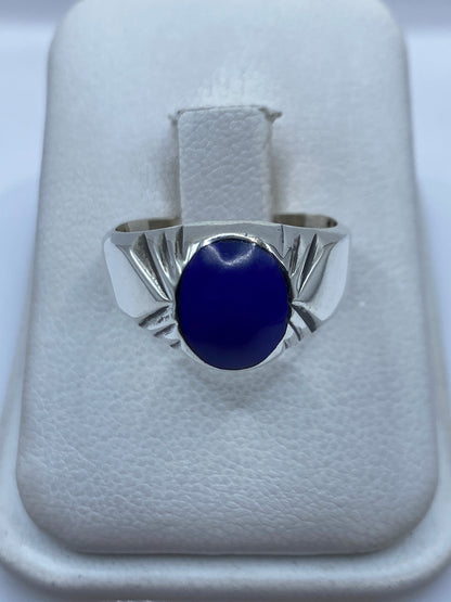 Anillo de plata con piedra azul engastada, visto de frente sobre dedo con manicura neutra