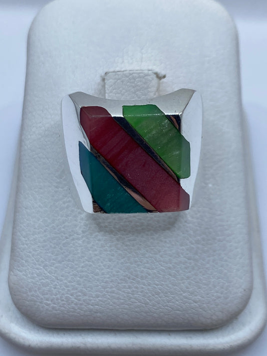 Anillo de plata con incrustación multicolor de piedras rojo, verde y azul teal sobre fondo blanco