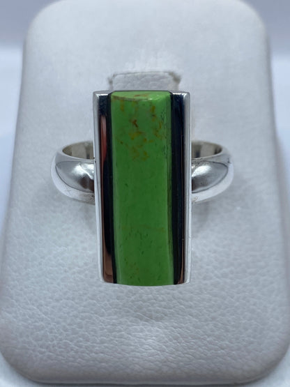 Anillo de plata minimalista con piedra verde rectangular en la mano de una mujer