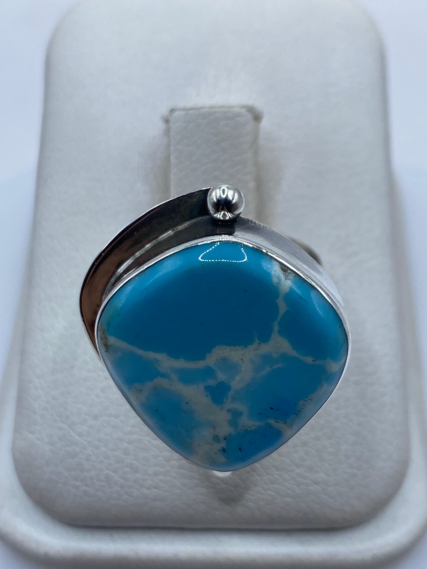 Anillo de plata ajustable con piedra azul cielo en expositor blanco, vista frontal del diseño
